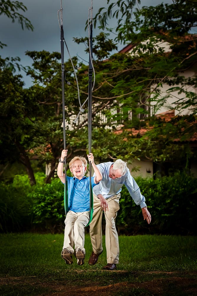 Tamarindo family photography – grand father pushing son on swing in tropical garden