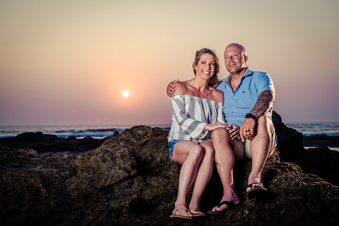 Tamarindo sunset beach portrait – couple sitting on rocks by the ocean