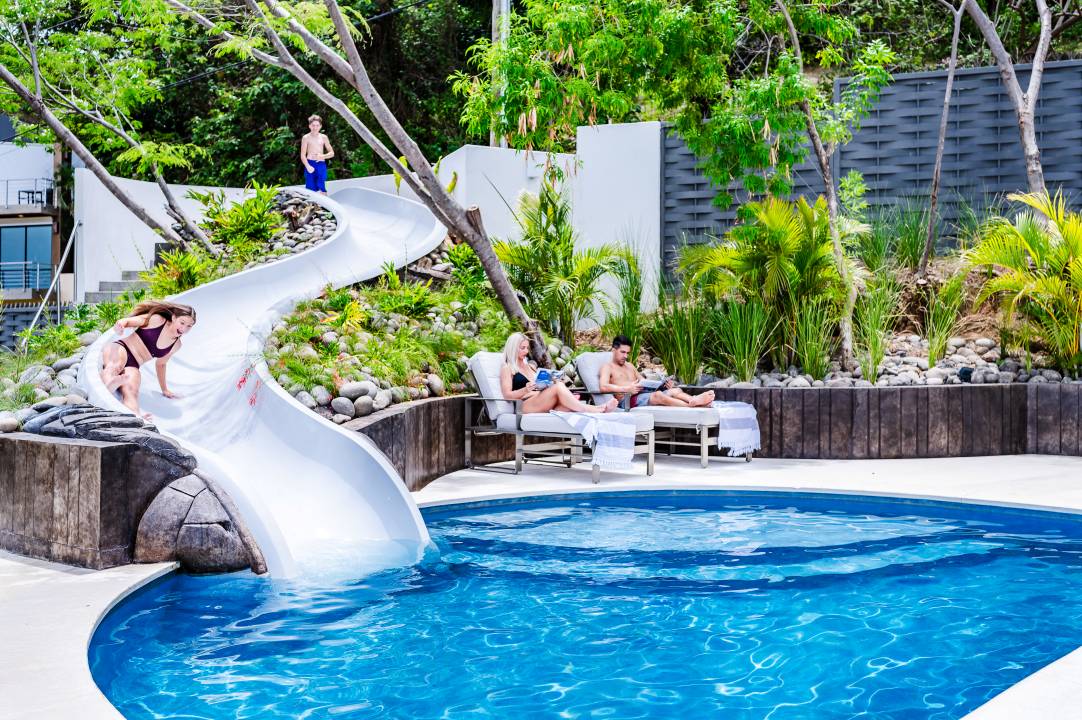 Lifestyle photography Costa Rica – kids enjoying tropical pool with slide surrounded by greenery